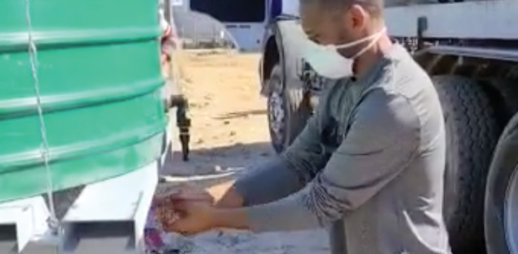Man in mask washing hands at a hand-washing station.